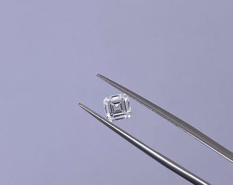 May include: A square-cut, clear diamond is held by silver tweezers against a light purple background. The diamond's facets reflect light, showcasing its brilliance. The tweezers are angled, presenting the gemstone for inspection.