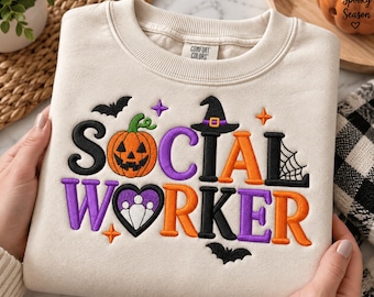 Puede incluir: Una sudadera de cuello redondo color crema con el texto bordado SOCIAL WORKER. El diseño incluye una calabaza, un sombrero de bruja, un corazón con un icono de tres personas, murciélagos, estrellas y una telaraña en negro, naranja y morado.