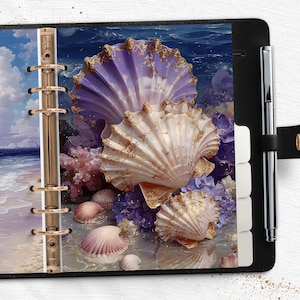 May include: Black planner with a seashell design. The planner features a gold-colored binding and a pen. The seashell design includes a large, light purple shell with gold trim, and several smaller, white and pink shells.