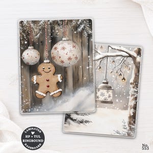 May include: Two rectangular laminated planner dashboards featuring winter illustrations. One shows a gingerbread person and two white ornaments hanging against a wooden fence. The other depicts a snowy tree with a hanging lantern and lights.