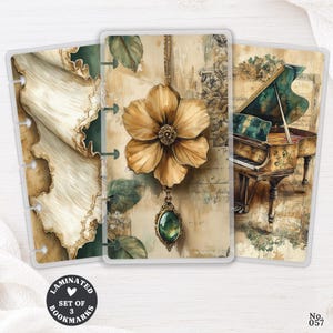 May include: A set of three laminated bookmarks featuring vintage-style illustrations. One bookmark shows draped fabric, another displays a large golden flower pendant with a green gemstone, and the third depicts a grand piano on a musical score background.