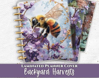May include: A set of laminated planner covers featuring a bee hovering over purple flowers, a wooden barrel filled with blossoms, purple orchids with water droplets, and a vintage compass. The covers are bound with gold-colored discs.