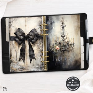 May include: A black ring-bound planner featuring a silver pen and two internal pages. The left page displays a large black bow illustration, while the right page shows a detailed chandelier with a single peach rose. Text reads No. 575 and PRINTABLE HP + TUL RINGBOUND DASHBOARD.