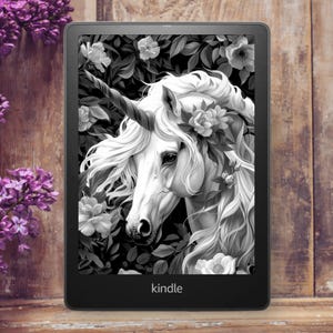 Peut inclure: Une illustration en noir et blanc d'une licorne avec une corne et des fleurs dans sa crinière. L'image est affichée sur une liseuse Kindle.