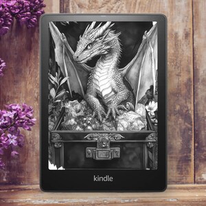 May include: A black Kindle e-reader displaying a detailed grayscale illustration of a dragon perched atop a treasure chest. The dragon has large wings and is surrounded by foliage. The word "kindle" is printed at the bottom.