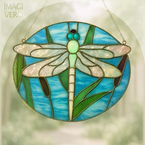 Pode incluir: Vitral de uma libélula. A libélula tem asas e corpo brancos, azul claro e verdes. O fundo é um oval azul com juncos verdes. Está pendurado por uma corrente. O texto "IMAGI VERO" está no canto superior esquerdo.