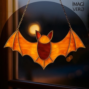Puede incluir: Decoración de murciélago de vidriera en tonos naranja y marrón. El murciélago está suspendido por una cadena y presenta alas detalladas. La imagen está sobre un fondo oscuro, con el texto "IMAGI VERO" visible.