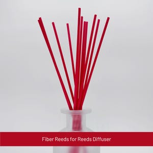 May include: A collection of bright red fiber reeds in a frosted glass diffuser bottle. The reeds are arranged in a fan shape, with the text "Fiber Reeds for Reeds Diffuser" in a red banner at the bottom.