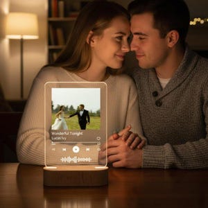 May include: A rectangular, illuminated acrylic night light with a wooden base. The light displays a photo of a couple and the text "Wonderful Tonight Lucas Ivy". The light has a music player interface with play, pause, and volume controls.