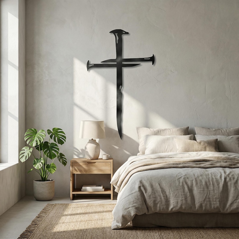 May include: A black metal cross wall art piece. The cross is made of stylized nails, with a vertical nail forming the main body and horizontal nails creating the cross arms. The artwork is mounted on a light-colored wall, above a bed.