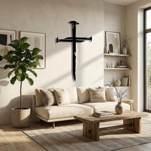 May include: A black metal cross sculpture with nail head details is mounted on a cream-colored wall. The cross is a minimalist design, suitable for home decor. The sculpture is displayed above a beige sofa.