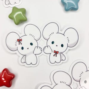 May include: White mouse stickers with black outlines and red bow ties. The stickers have large round ears and small arms. Scattered around the stickers are green, blue, and red star-shaped embellishments.