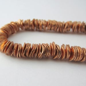 May include: A copper-colored necklace made of small, flat, wavy discs. The necklace is made of many individual pieces that are strung together.