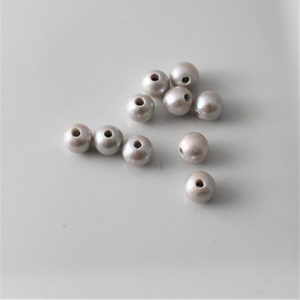 May include: A group of ten off-white round beads with a hole in the center. The beads are scattered on a light gray surface.