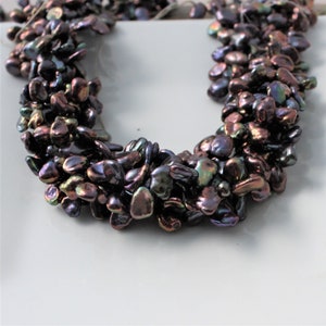 May include: A strand of iridescent black freshwater pearls, strung together in a loose, cascading style. The pearls are irregular in shape and size, creating a unique and textured look.