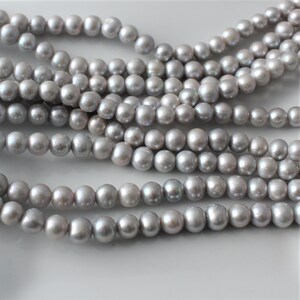 May include: A strand of gray pearl beads. The pearls are round and smooth, and they have a slight iridescent sheen.