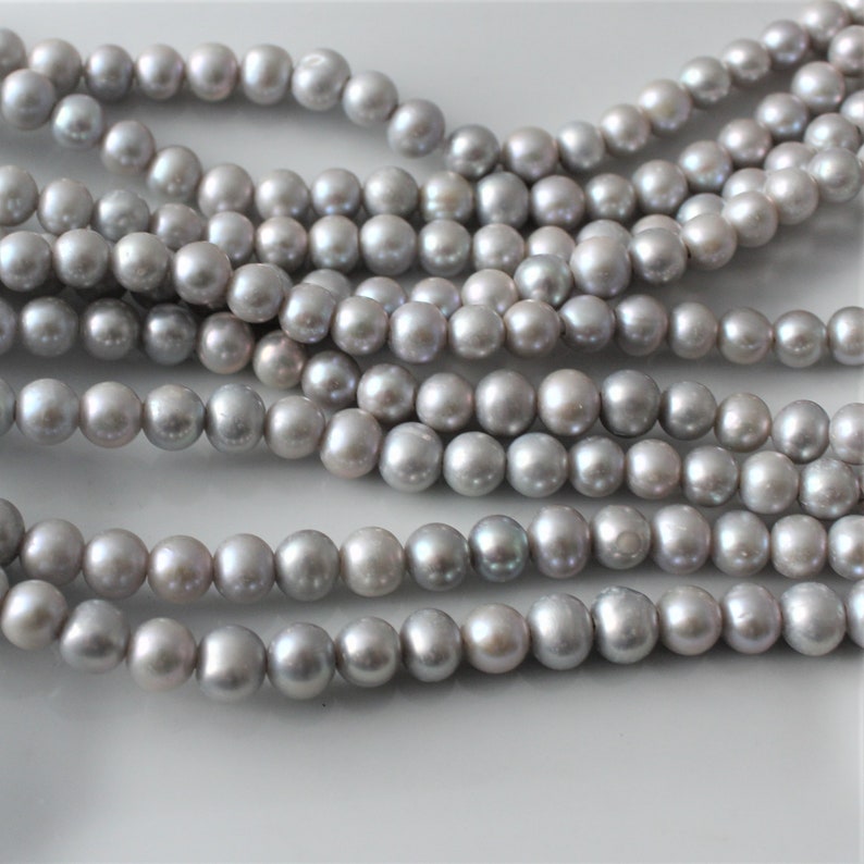 May include: A strand of gray pearl beads. The pearls are round and smooth, and they have a slight iridescent sheen.