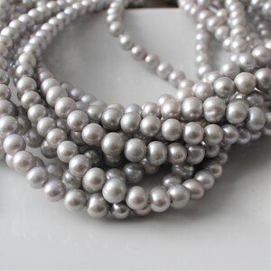 May include: A strand of gray pearl beads. The pearls are round and smooth, and they are strung on a clear thread.