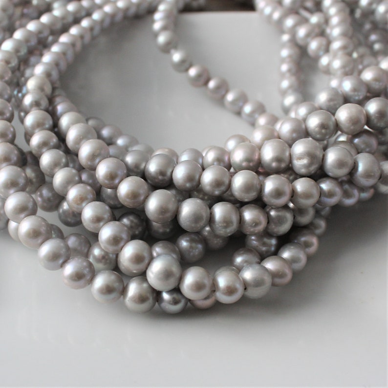 May include: A strand of gray pearl beads. The pearls are round and smooth, and they are strung on a clear thread.