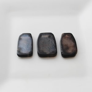 May include: Three black agate slices with a unique pattern of white and gray swirls. The slices are rectangular and have a smooth, polished surface.