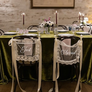 May include: Wedding reception table setting with a green velvet tablecloth, candles, and floral arrangements. Two chairs are decorated with lace and ribbons, with the words "Just" and "Married" displayed.