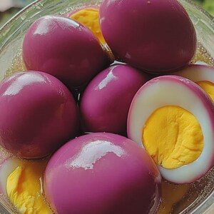 Peut inclure: Un bol en verre rempli d'œufs marinés violets vibrants. Certains œufs sont entiers, tandis que d'autres sont coupés en deux, révélant des jaunes d'œufs jaune vif. Les œufs sont immergés dans un liquide clair. En arrière-plan, un paysage de montagne.