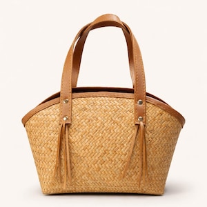 May include: A woven straw tote bag with brown leather handles and trim. The bag has a rectangular shape with a curved top and decorative leather tassels. The brand "BORNEO -WEAVE CO.-" is printed on the upper left.