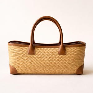 May include: A rectangular woven straw tote bag with brown leather handles, trim, and corner accents. The bag has a zip closure and the text "BORNEO -WEAVE CO-" is visible on the upper left corner.