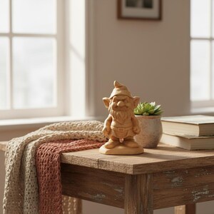 May include: A wooden garden gnome figurine with a pointed hat, beard, and belt stands on a rustic wooden table. A beige and pink knitted throw and a potted succulent are also on the table. A window and books are in the background.