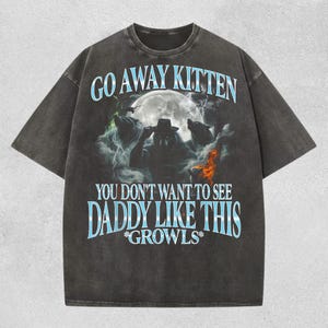 May include: Dark gray t-shirt with a graphic design featuring a werewolf, wolves, and the text "GO AWAY KITTEN, YOU DON'T WANT TO SEE DADDY LIKE THIS *GROWS*". The design includes a full moon and lightning.