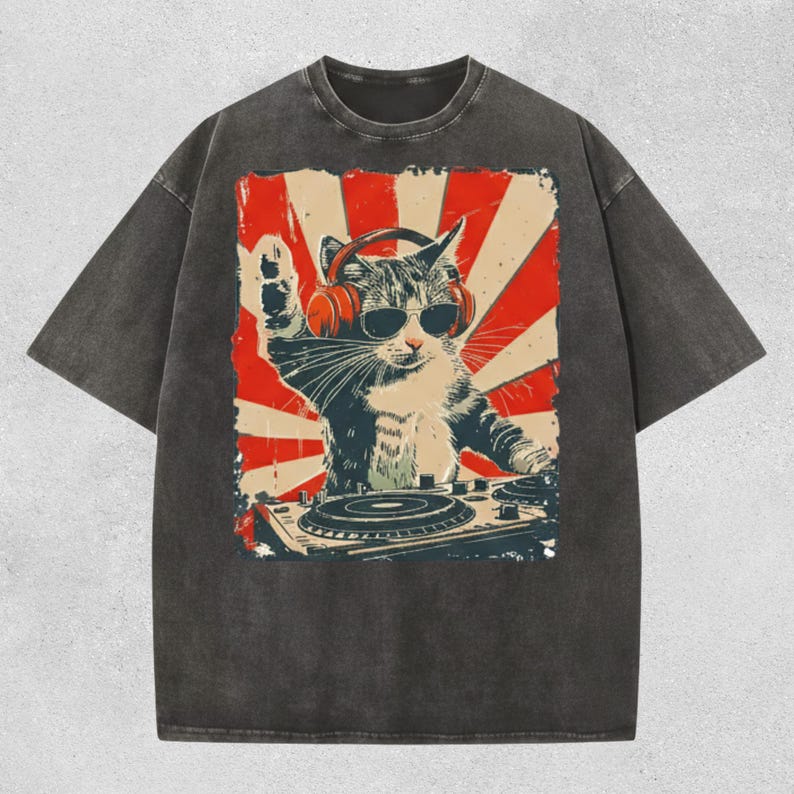Puede incluir: Camiseta gris oscuro con un gato DJ con gafas de sol y auriculares, con un dise&ntilde;o de rayos de sol rojo y blanco en el fondo. El gato est&aacute; detr&aacute;s de una mesa de mezclas, con una pata levantada.