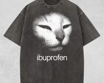 May include: Dark gray t-shirt featuring a distressed white cat face graphic. The word "ibuprofen" is printed in white below the cat's face. The shirt has short sleeves and a crew neck.