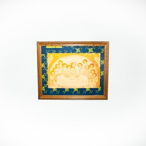 May include: A framed painting depicting a religious scene with multiple figures in a light brown colour scheme. The frame is made of wood with a dark brown finish. The painting is set against a white wall.