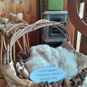 May include: A wicker basket filled with white 100% Ladakhi Pashmina Fleece, priced at $30 per 50g. The basket is sitting on a wooden surface.