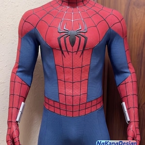 Puede incluir: Un traje de cuerpo completo texturizado en rojo y azul con un emblema de araña negro en el pecho, un patrón de telaraña negro en las secciones rojas y accesorios plateados en las muñecas. El texto NgKangDesign es visible abajo a la derecha.