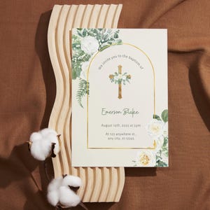 May include: Baptism invitation card with floral and cross design. The card features the text "We invite you to the baptism of Emerson Blake" and event details. The card is decorated with white roses and greenery.