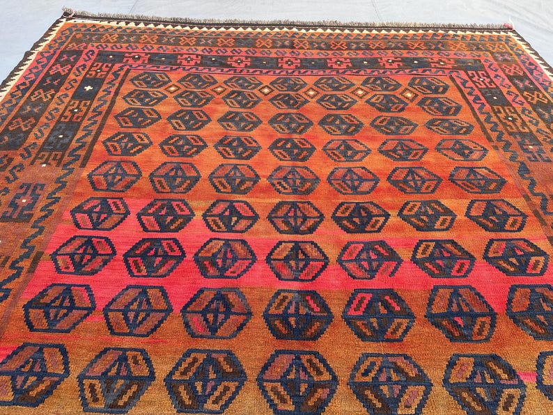 May include: A rectangular rug with a geometric pattern. The rug features a repeating pattern of dark blue and brown geometric shapes on a red and orange background. The border is a darker brown with geometric designs.