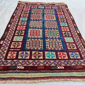 May include: A rectangular area rug featuring a deep blue central field filled with a grid of multicolored square motifs in red, teal, and purple. The border displays a geometric pattern in tan, red, and black, finished with a fringed edge.