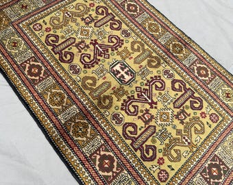 Könnte beinhalten: Rechteckiger Teppich mit einem zentralen Feld in Beige und aufwendigen geometrischen Mustern in Burgunderrot, Braun und Gold. Der Teppich hat einen detaillierten Rand mit sich wiederholenden Motiven und einen schwarzen Rand. Traditioneller, dekorativer Bodenbelag.