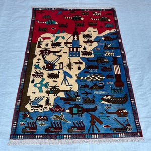 May include: A rectangular area rug featuring a map of Pakistan in cream, set against a red and blue background. The design includes various military vehicles, helicopters, jets, and artillery icons, with the word PAKISTAN printed in white.