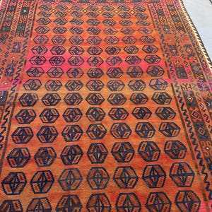 May include: A rectangular rug with a geometric pattern in shades of orange, red, and navy blue. The central design features repeating hexagonal shapes. The rug has a detailed border with various patterns and colours.