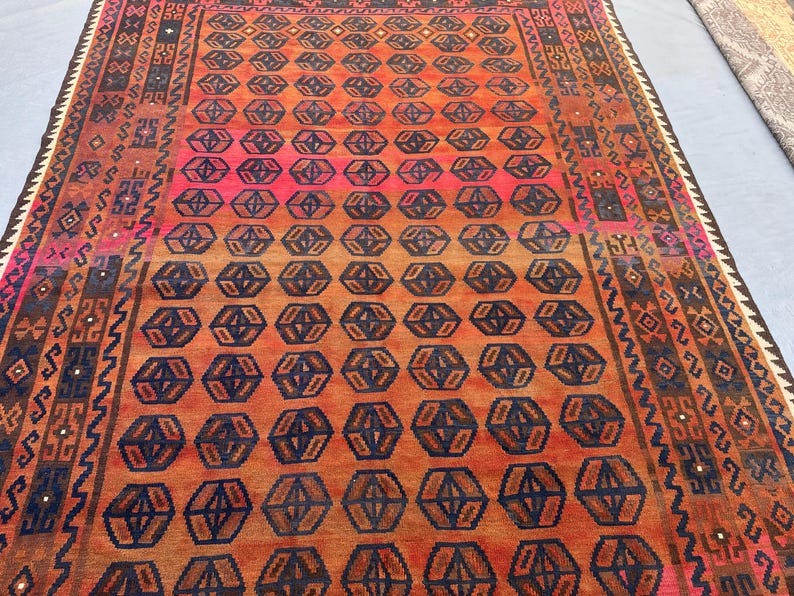 May include: A rectangular rug with a geometric pattern in shades of orange, red, and navy blue. The central design features repeating hexagonal shapes. The rug has a detailed border with various patterns and colours.