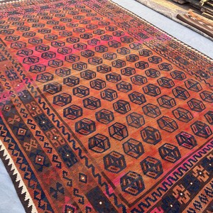 May include: A rectangular, hand-woven rug with a geometric pattern. The rug features a central field of repeating dark blue and brown geometric shapes on an orange and pink background. The border has a dark blue and brown design.