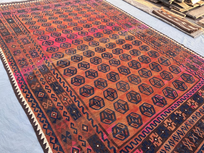 May include: A rectangular, hand-woven rug with a geometric pattern. The rug features a central field of repeating dark blue and brown geometric shapes on an orange and pink background. The border has a dark blue and brown design.