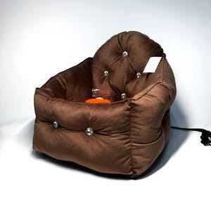 May include: A brown velvet pet bed with a tufted design and crystal-like buttons. The bed has a square shape and a rounded top.