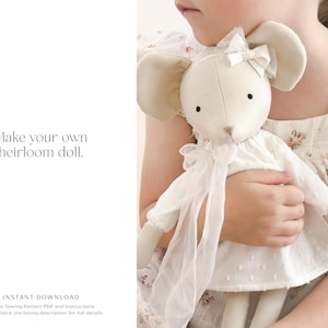 K&ouml;nnte beinhalten: Eine cremefarbene Mauspuppe mit gro&szlig;en, abgerundeten Ohren und einem wei&szlig;en Kleid wird von einer Person gehalten. Die Puppe hat eine Schleife auf dem Kopf und einen langen, flie&szlig;enden Schal. Der Text "Make your own heirloom doll" ist sichtbar.