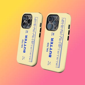 May include: Two phone cases with a butter-themed design. The cases are light yellow with blue text that reads "SALTED BUTTER" and a measurement chart. The cases have a black camera and button details.