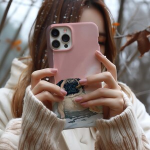 May include: A pink phone case featuring a pug dog design. The case has a smooth finish and a detailed illustration of a pug with a cigar. The phone case has a camera cutout and button placements.