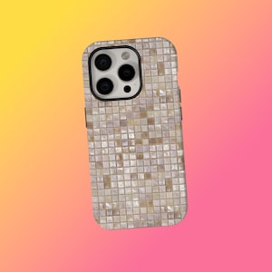 Puede incluir: Una funda de teléfono inteligente con un diseño de mosaico. La funda está cubierta de pequeñas baldosas cuadradas en tonos beige, crema y marrón claro. Las lentes de la cámara del teléfono son visibles en la parte superior. El fondo es un degradado de amarillo y rosa.