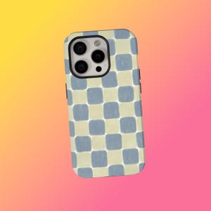 May include: A smartphone case featuring a blue and cream chequered design. The case has a camera aperture and black side buttons. The background is a gradient of yellow, orange, and pink.